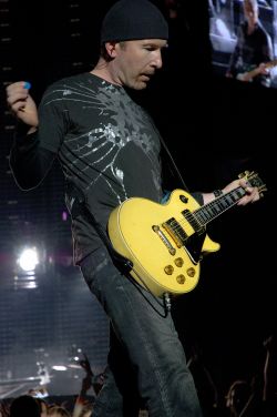 The Edge - ´muž tisíce kytar´; v pozadí na obrazovce baskytarista Adam Clayton